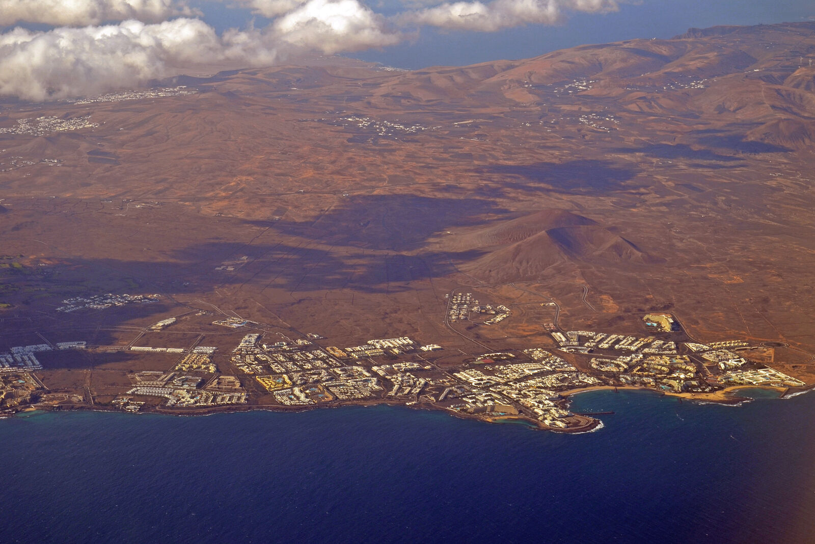 Aerial of Costa Teguise with low-rise white buildings, palm-lined streets and the Atlantic