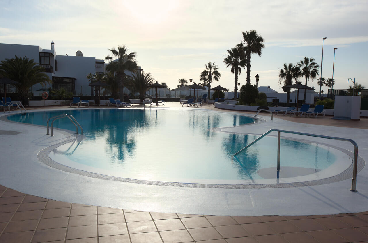 Crescent-shaped communal pool with palm trees and sun loungers at the Nazaret residential community, 2 minutes on foot from Casa Los Alisios