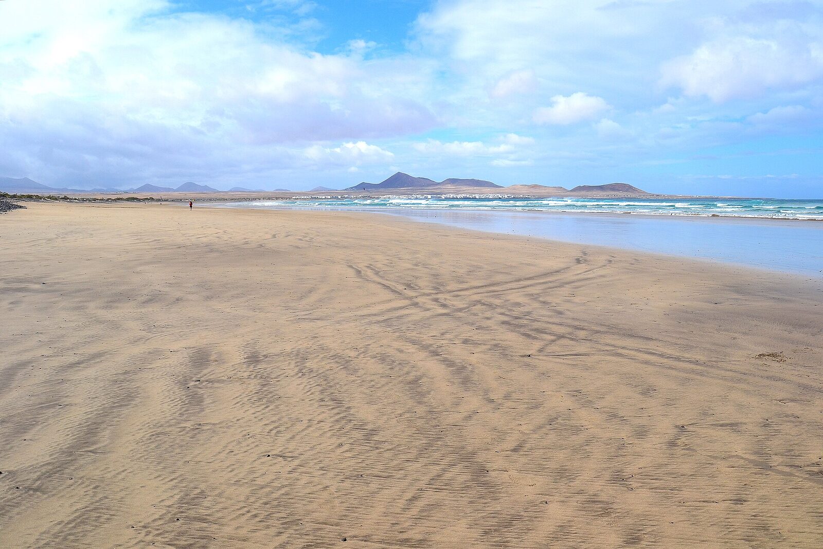 The wide sand beach at Playa de Famara at low tide, with the village of Caleta de Famara in the distance