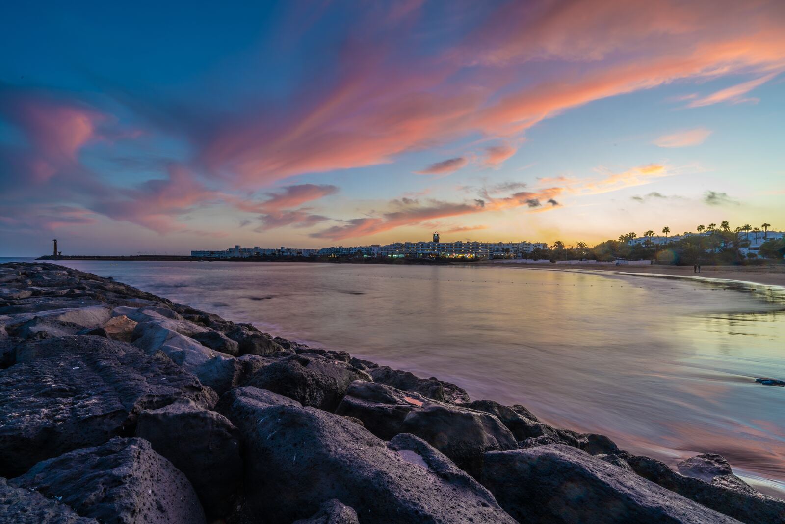 Sunset over the bay at Costa Teguise in summer with the resort skyline and rocky breakwater, Lanzarote