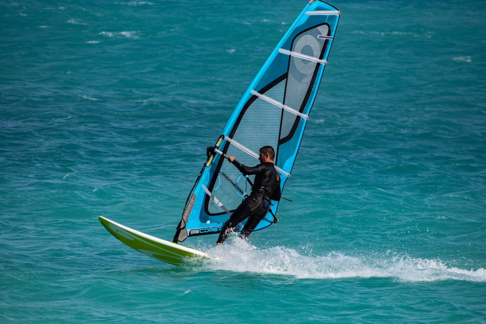 Windsurfer on a teal board carving in clear water under a blue sail